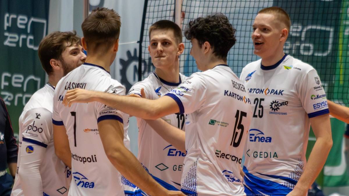 Drużyna siatkarzy w białych strojach świętuje zwycięstwo na boisku.