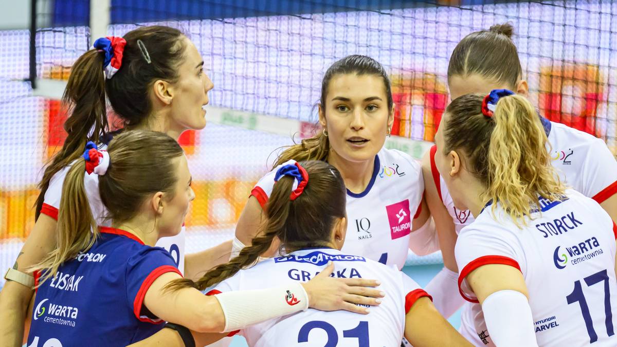 Grupa siatkarek w białych strojach sportowych, świętująca na boisku.