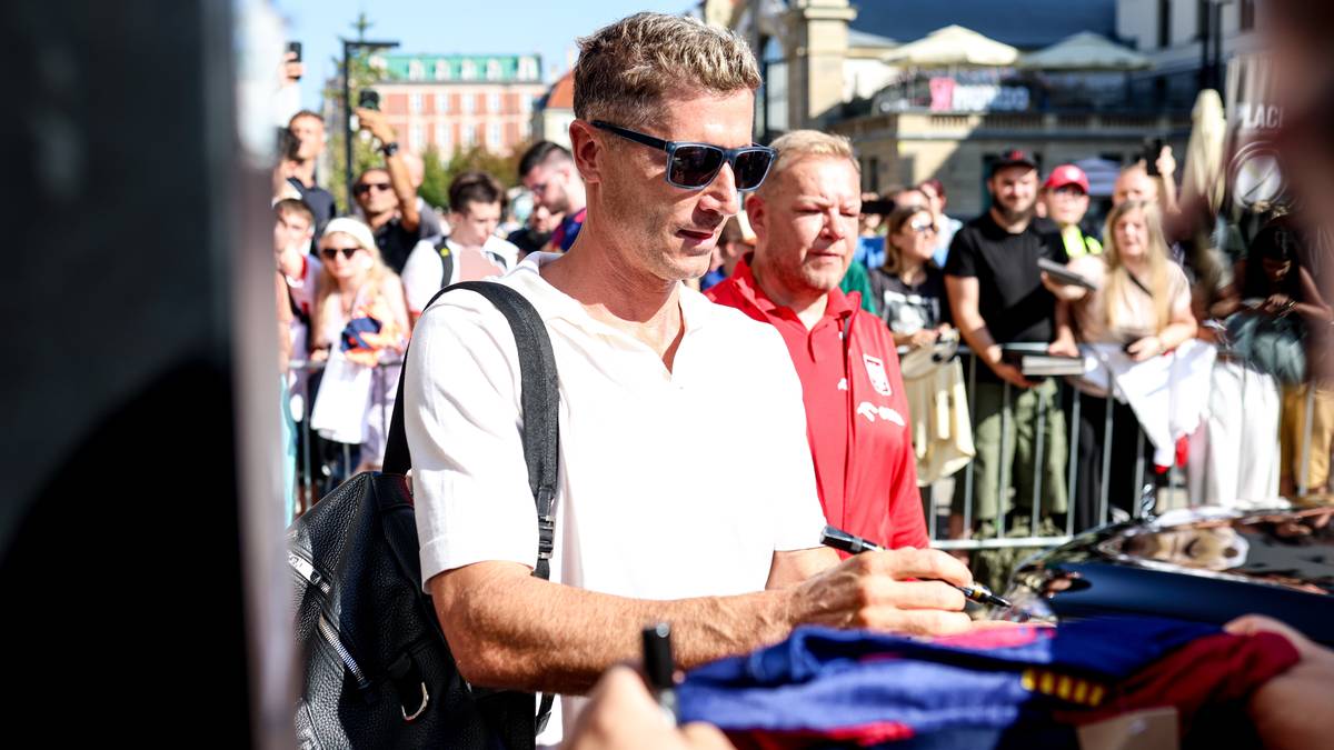 Robert Lewandowski podpisuje koszulkę na tle grupy fanów.