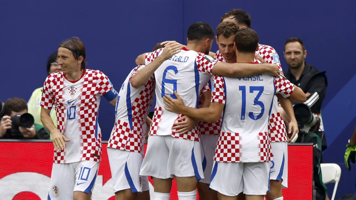 Piłkarze reprezentacji Chorwacji w białych strojach z czerwonymi elementami, czołgający się w radosnym uścisku po zdobyciu bramki. Na boisku panuje atmosfera sportowej rywalizacji.