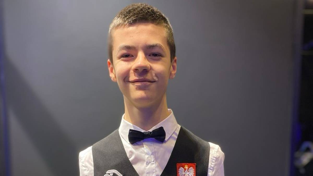 Portret młodego mężczyzny w stroju do snookera, z uśmiechem na twarzy.