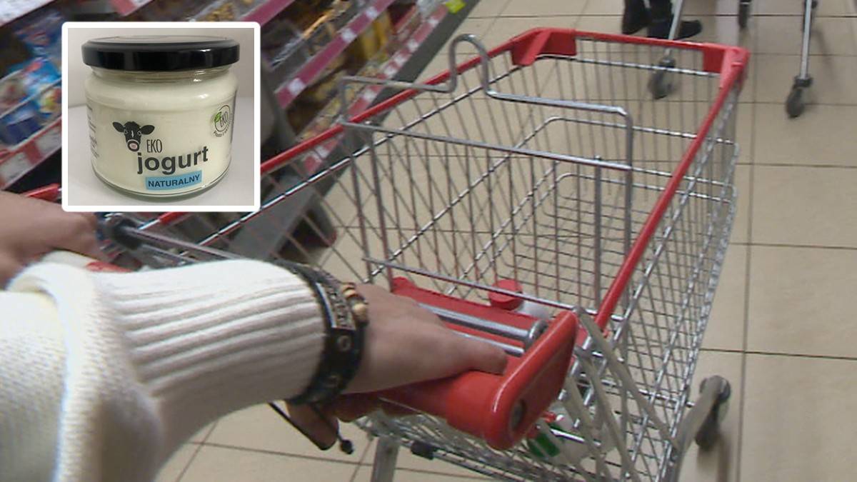 Zbliżenie na słoik z jogurtem naturalnym w rogu obrazka, obok w&oacute;zek sklepowy.
