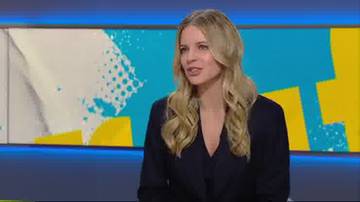 Kobieta z blond włosami w czarnej marynarce siedzi przed ekranem z niebiesko-ż&oacute;łtym wzorem.