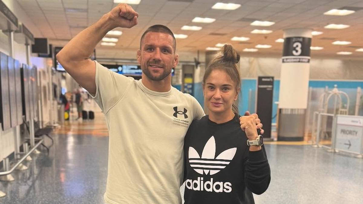 Sportowcy Mateusz Gamrot i Mateusz Kowalkiewicz pozują do zdjęcia w lotniskowym terminalu.