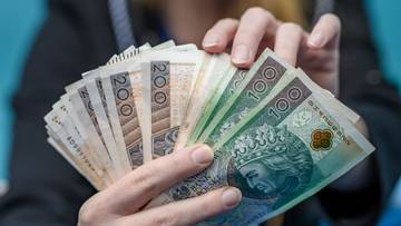 Dłonie trzymające stos polskich banknot&oacute;w o nominałach 100 i 200 zł.