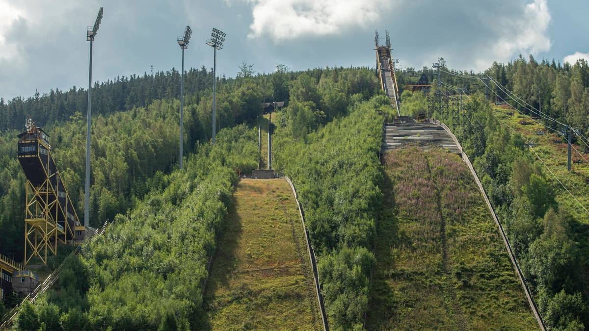 Kompleks skoczni narciarskich "Certak" w Harrachovie z widocznymi wieżami najazdu i zalesionym wzg&oacute;rzem w tle.