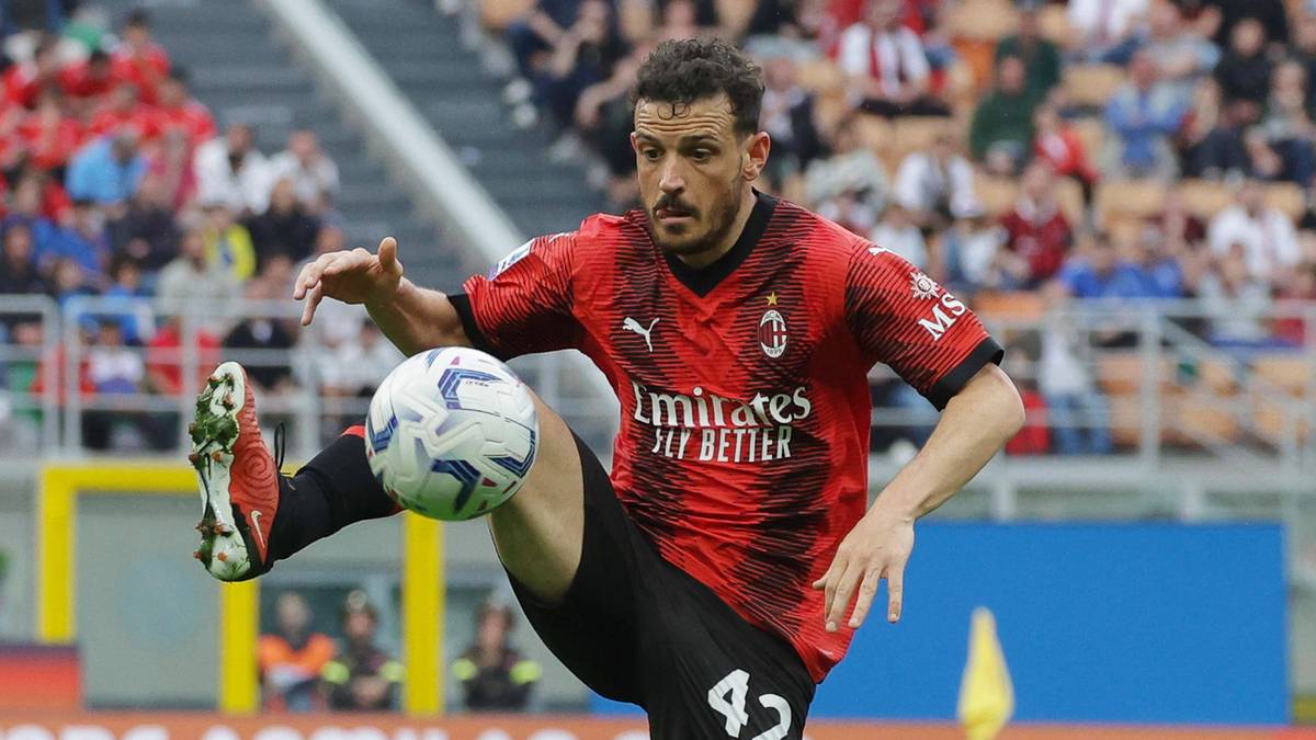 Piłkarz w czerwonej koszulce z czarnymi pasami kopie piłkę.