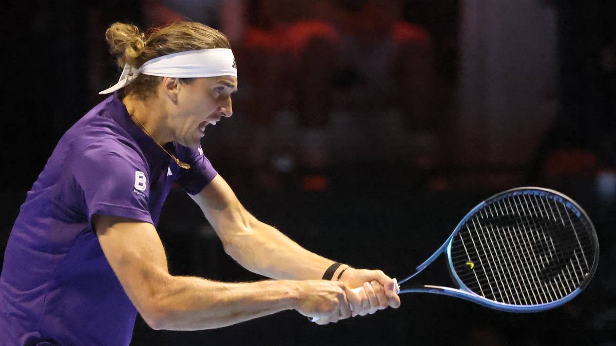 Tenisista w fioletowej koszulce i białej opasce na głowie, zacięty w uderzeniu rakietą tenisową.