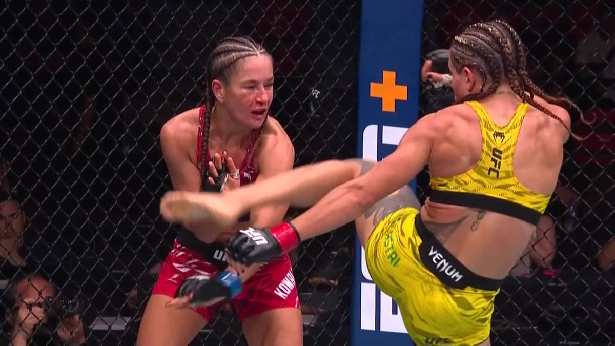 Dwóch kobiet walczących w oktagonie UFC. Jedna zawodniczka w czerwonym stroju wykonuje kopnięcie w kierunku drugiej, która jest w żółtym stroju.