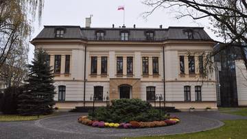 Elegancki, piętrowy budynek administracyjny o jasnej fasadzie, z ciemnym dachem i polską flagą na dachu.