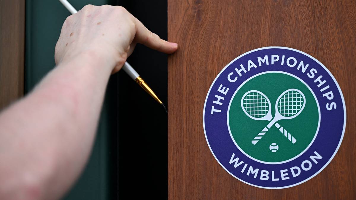 Dłoń z pędzlem zbliża się do okrągłego logo Wimbledonu.