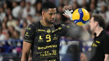 Siatkarz w czarnej koszulce z numerem 9 i ż&oacute;łto-niebieskiej piłce w dłoni.