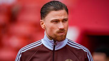 Portret piłkarza w bordowej bluzie z białymi pasami na rękawach i kołnierzykiem.