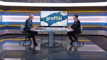 Dw&oacute;ch mężczyzn w garniturach siedzi naprzeciwko siebie przy okrągłym stole w studiu telewizyjnym. Na ekranie za nimi widnieje napis "graffiti".