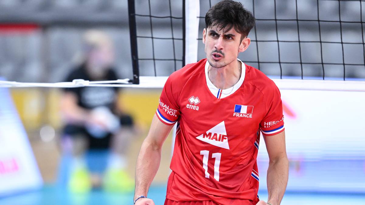 Siatkarz w czerwonej koszulce z numerem 11 i francuską flagą, z wyrazem skupienia na twarzy, na boisku siatkarskim.