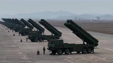 Rząd samobieżnych wyrzutni rakietowych ustawionych w szeregu na pustym terenie, z g&oacute;rami w tle. Kilku żołnierzy stoi obok pojazd&oacute;w.