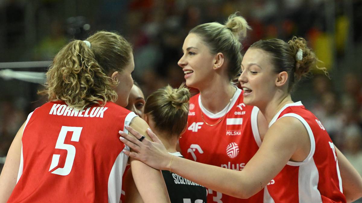 Cztery zawodniczki drużyny w czerwonych strojach z białymi napisami, rozmawiają ze sobą podczas meczu siatkówki. Widoczne numery na koszulkach: 5 i częściowo 13. Jedna z zawodniczek delikatnie obejmuje drugą.