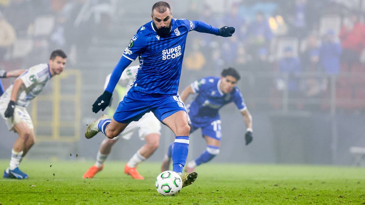 Piłkarz w niebieskiej koszulce Lech Poznań prowadzi piłkę na murawie, pr&oacute;bując ominąć przeciwnika.