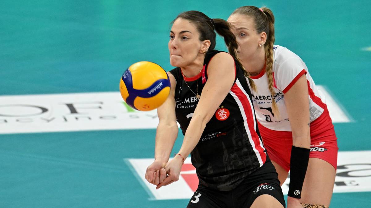 Siatkarka w czarnym stroju odbija piłkę, siatkarka w białej koszulce w tle.