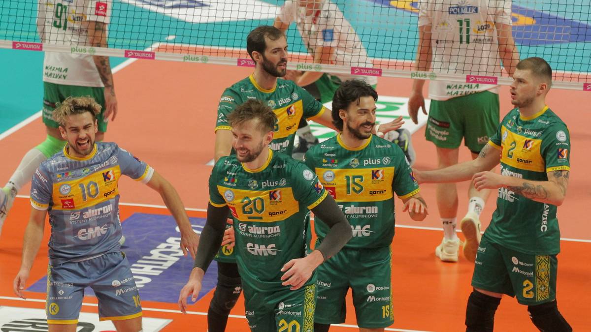 Siatkarze w zielonych i niebieskich strojach na boisku siatkarskim.