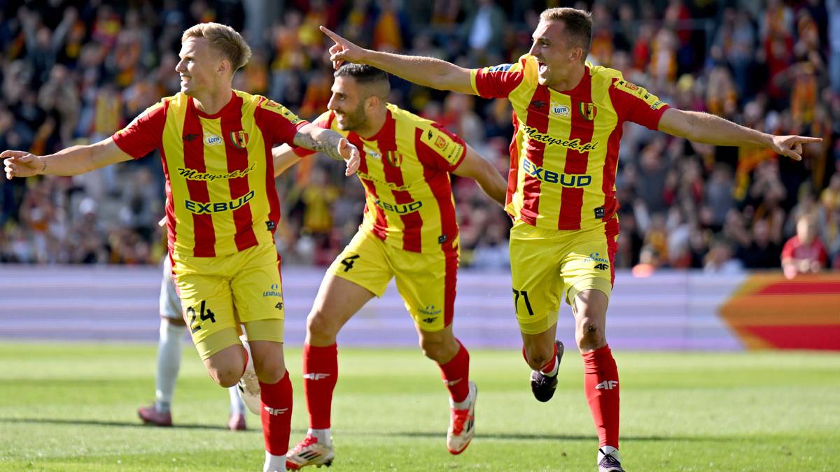 Trzech piłkarzy Korony Kielce w żółto-czerwonych strojach świętuje zdobycie bramki na boisku piłkarskim.