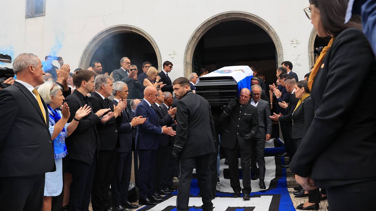 Kondukt pogrzebowy z trumną ozdobioną emblematami piłkarskimi, otoczony przez żałobnik&oacute;w w eleganckich strojach.