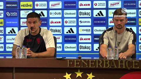 Dw&oacute;ch mężczyzn siedzi przy stole konferencyjnym z mikrofonami przed nimi. Za nimi znajduje się ściana z logo "Fenerbahce".