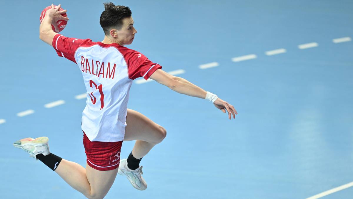 Piłkarka ręczna w białej koszulce z czerwonymi rękawami i numerem 31 oraz czerwonych spodenkach, w locie wykonuje rzut piłką.