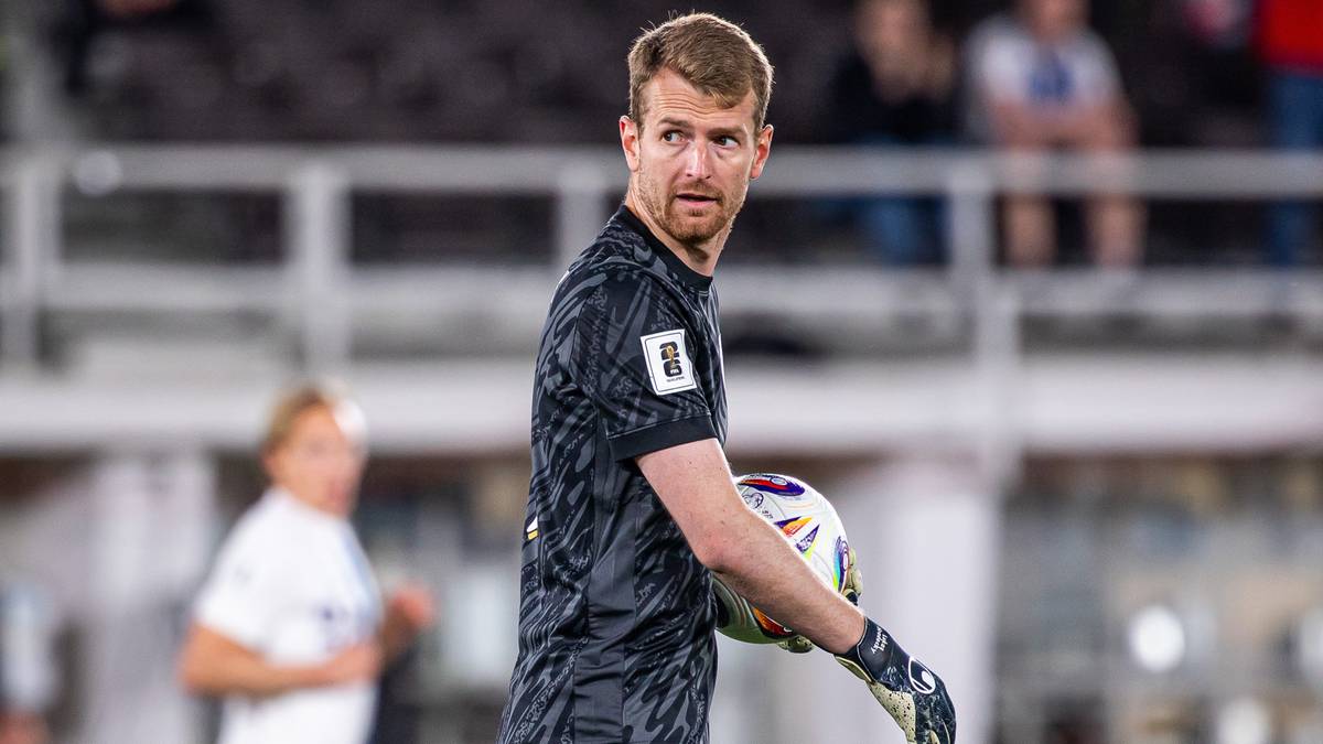 Młody bramkarz w czarnej koszulce piłkarskiej trzyma piłkę w ręku, patrząc w bok.