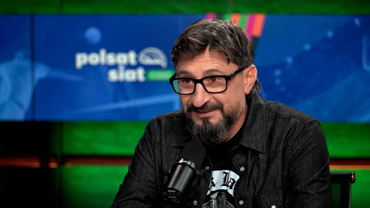 Mężczyzna z okularami i brodą siedzi przed mikrofonem w studiu telewizyjnym Polsat.