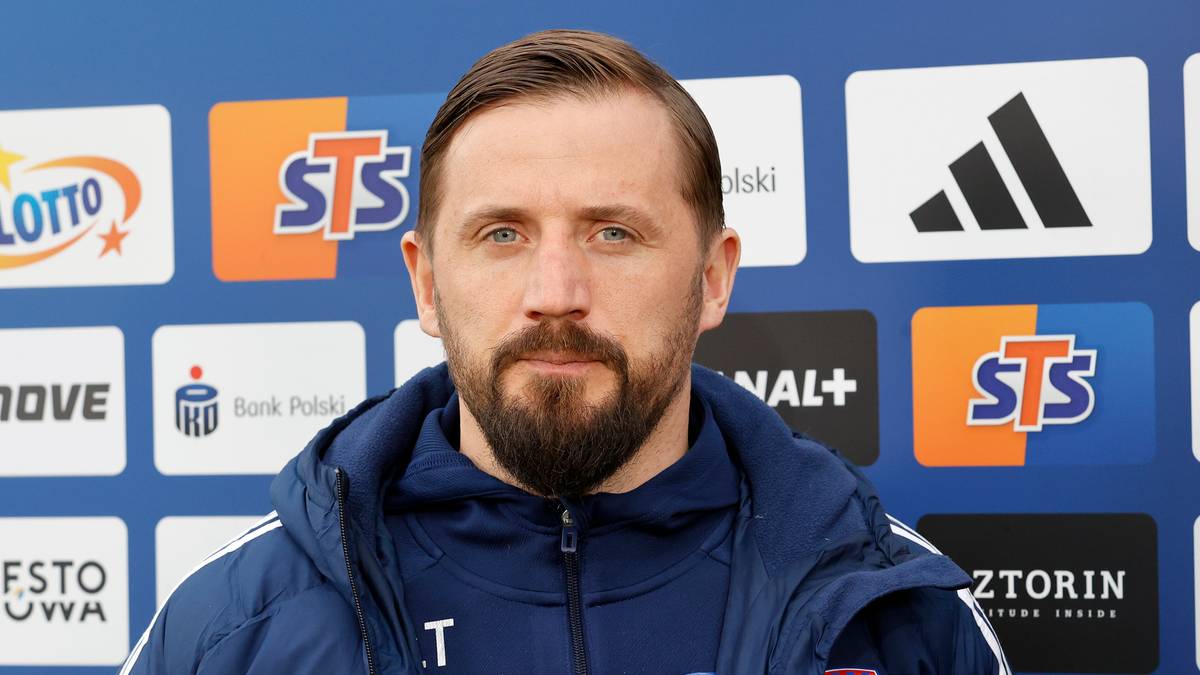 Portret mężczyzny z kr&oacute;tką brodą, ubranego w granatową kurtkę sportową z widocznym logo klubu.