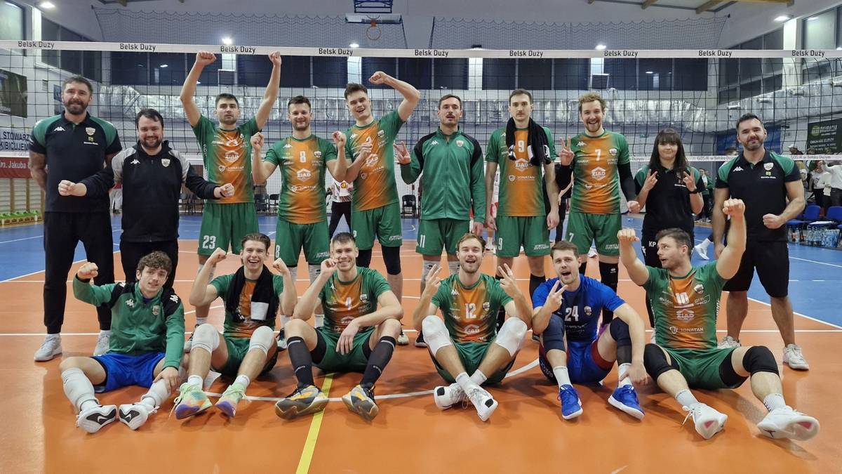 Siatkarze w strojach sportowych pozują do zdjęcia drużynowego na boisku.