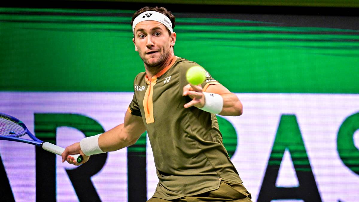 Tenisista w zielonej koszulce i opasce na głowie trzyma rakietę i piłkę tenisową, gotowy do zagrania.