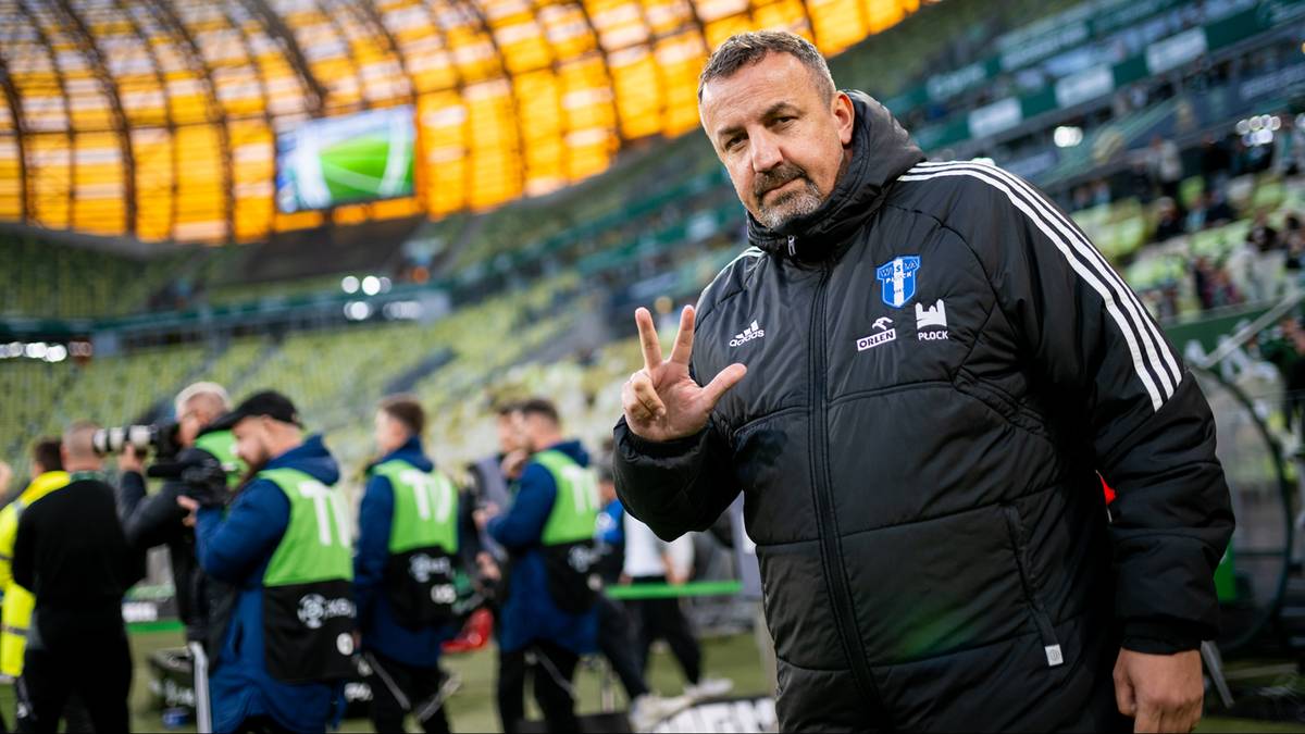 Trener Mariusz Misiura z Wisły Płock w kurtce z logo klubu gestykuluje na tle stadionu.