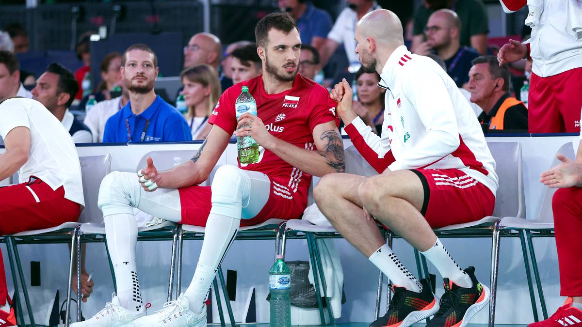 Dw&oacute;ch siatkarzy siedzi na ławce podczas meczu, jeden z nich trzyma butelkę z wodą.