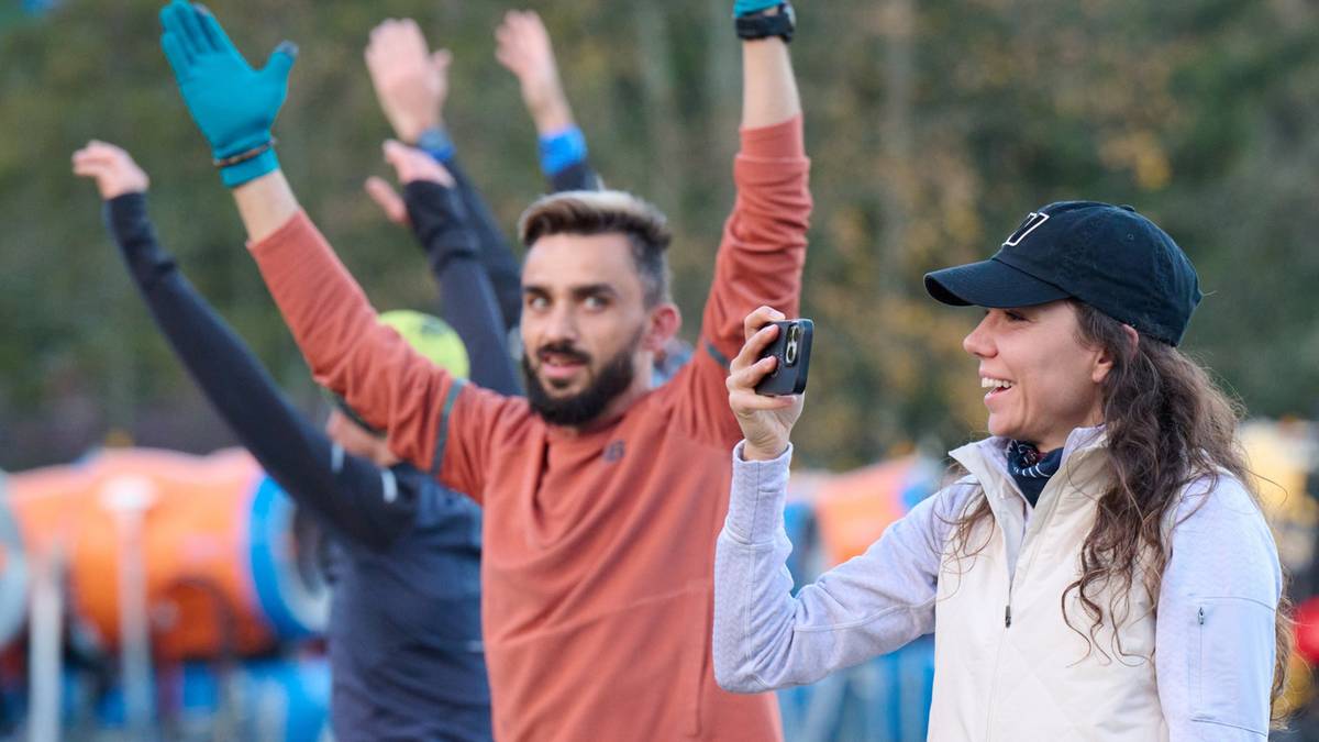 Grupa ludzi ćwiczących na świeżym powietrzu, z podniesionymi rękami w geście radości i wysiłku.