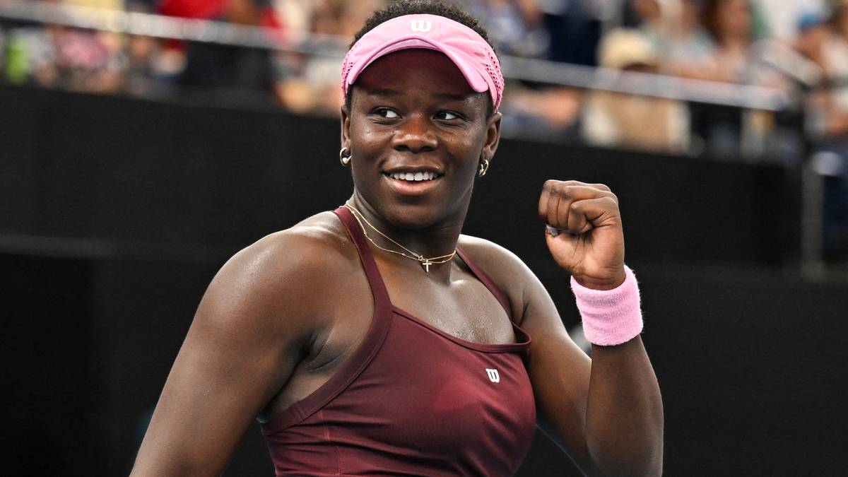 Tenisistka z ciemną karnacją w r&oacute;żowej opasce i sportowym stroju, radośnie unosi zaciśniętą prawą pięść.