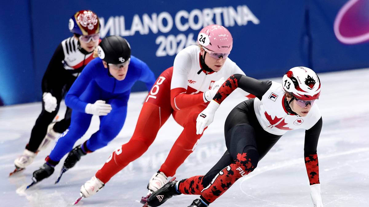 Zawodniczka w czerwonym stroju z białym orłem na piersi ślizga się po lodzie na łyżwach, wyprzedzając rywalkę w niebieskim stroju.