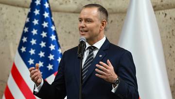 Mężczyzna w garniturze przemawia do mikrofonu, obok niego flagi Stan&oacute;w Zjednoczonych i Polski.