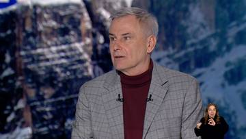 Mężczyzna w garniturze i golfie, na tle g&oacute;rskiego krajobrazu, z tłumaczem języka migowego w prawym dolnym rogu.