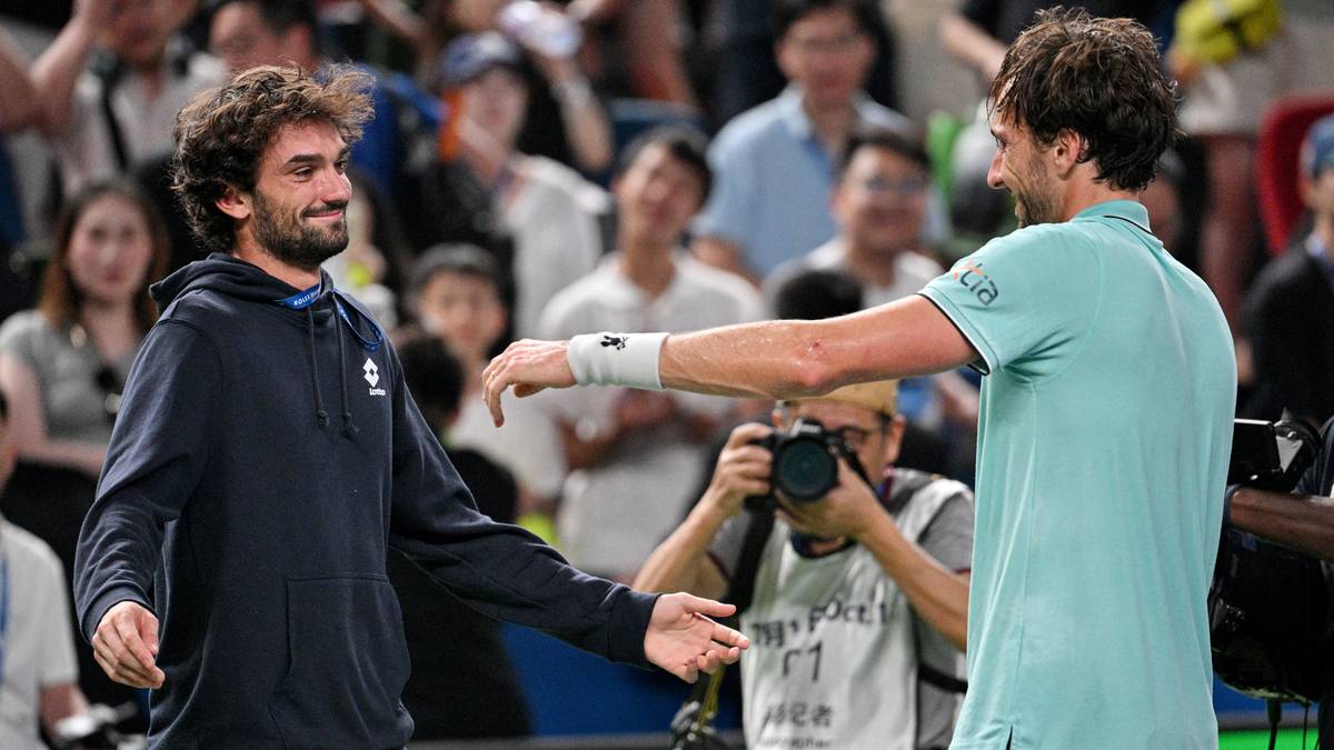 Dwóch białych mężczyzn w strojach sportowych ściska sobie dłonie na tle widowni.