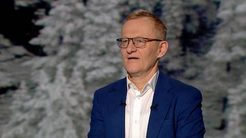 Portret mężczyzny w okularach i granatowej marynarce na tle zimowego krajobrazu.