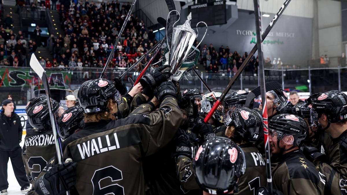 Hokeiści w czarnych strojach z uniesionym pucharem świętują zwycięstwo, trybuny wypełnione kibicami.