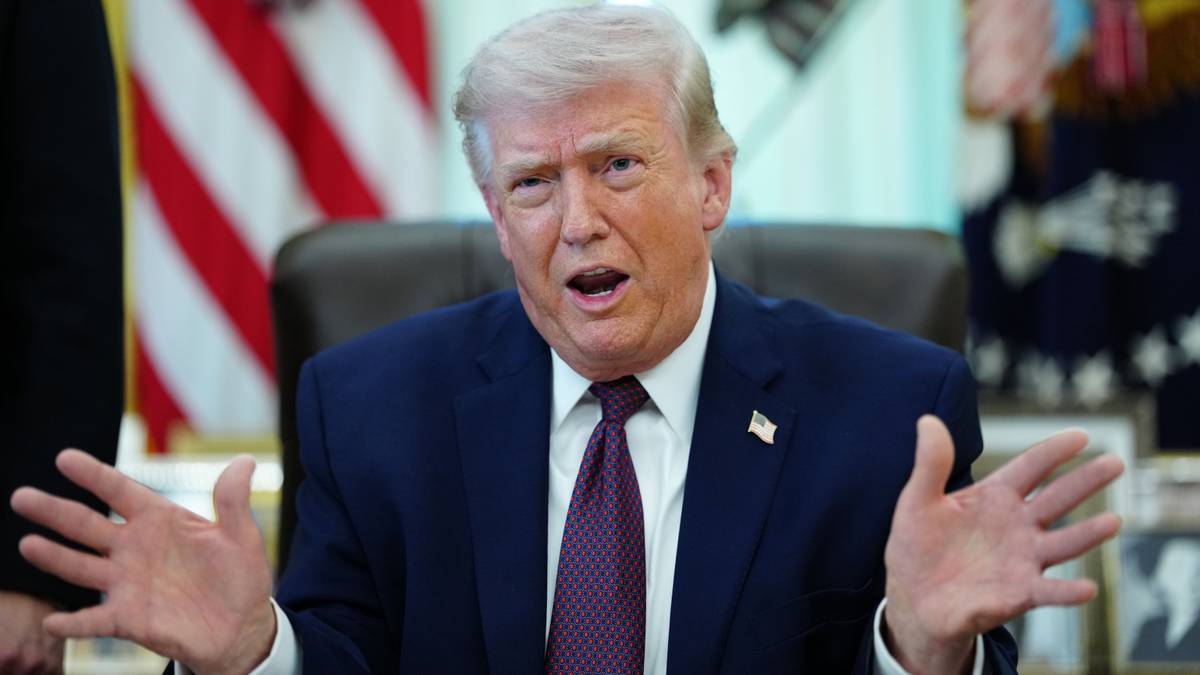 Donald Trump przemawia z otwartymi dłońmi, w garniturze i krawacie, na tle flagi USA.