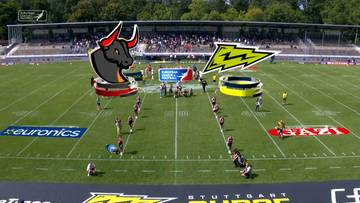 Boisko do futbolu amerykańskiego z logotypami Stuttgart Surge i Madrid Bravos, zawodnikami i trybunami.