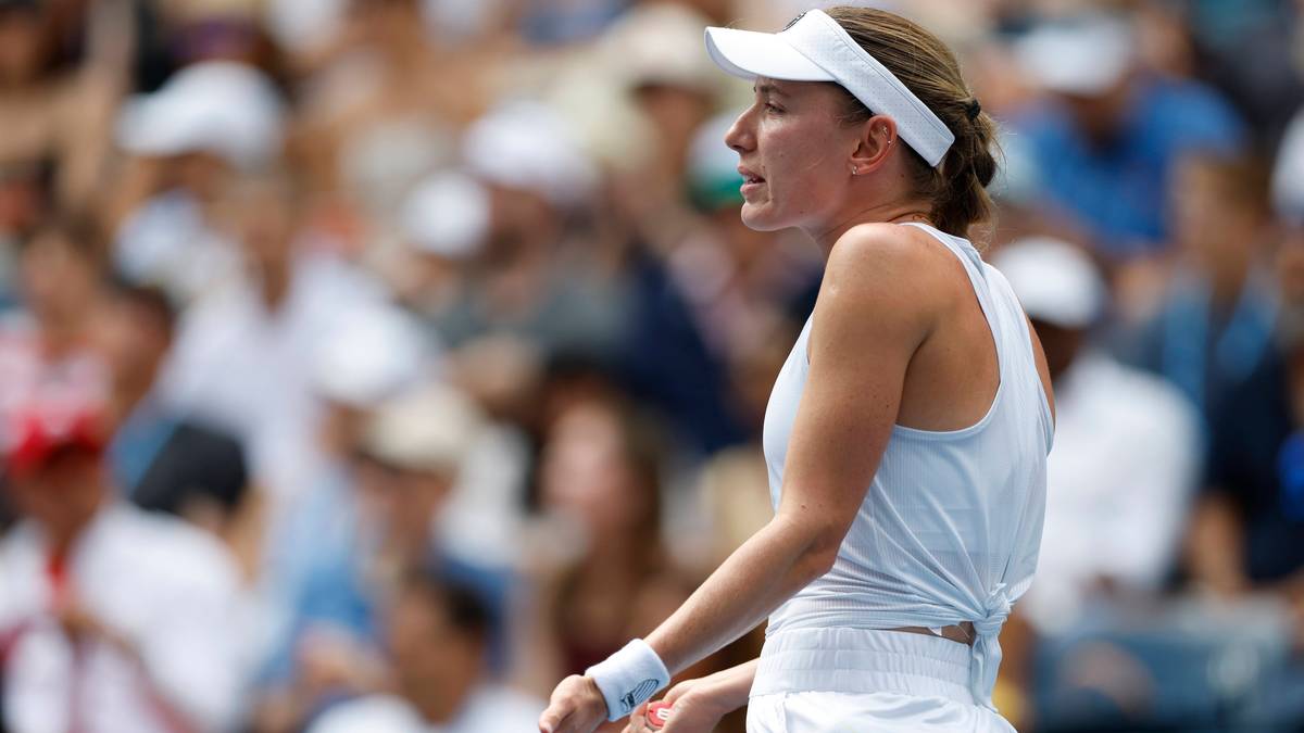 Zamyślona tenisistka w białej koszulce i czapce z daszkiem, w tle rozmyty tłum kibiców.