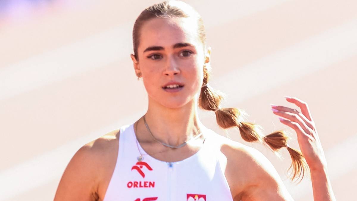 Młoda lekkoatletka w białej koszulce z napisem "ORLEN" i polskim orłem, z długimi blond włosami splecionymi w gruby warkocz, patrząca przed siebie z determinacją.