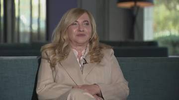 Portret kobiety z blond włosami w jasnym kostiumie siedzącej na kanapie.