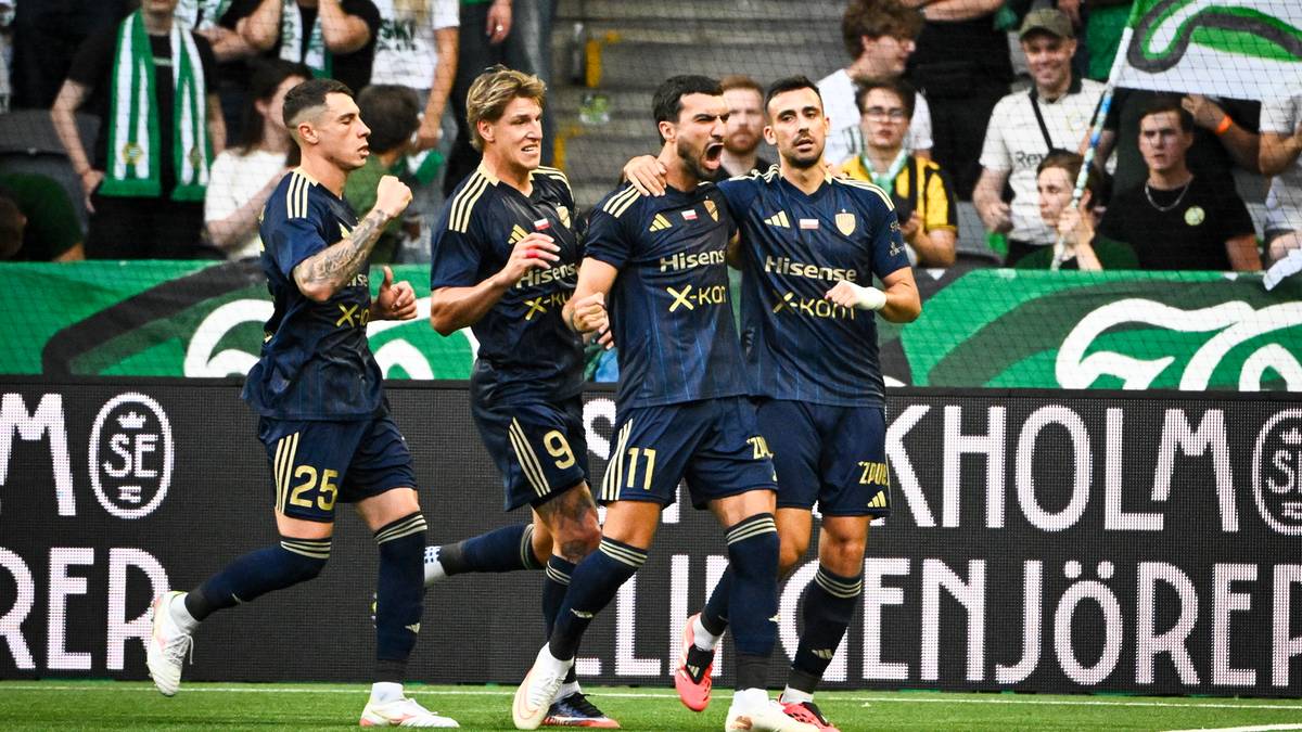 Pięciu piłkarzy w niebieskich strojach z numerami na plecach idzie po murawie stadionu, patrząc w kierunku widowni.