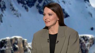 Kobieta w jasnobrązowej marynarce i czarnej bluzce z dekoltem w serek, patrząca w bok. W tle widać ośnieżone g&oacute;ry.